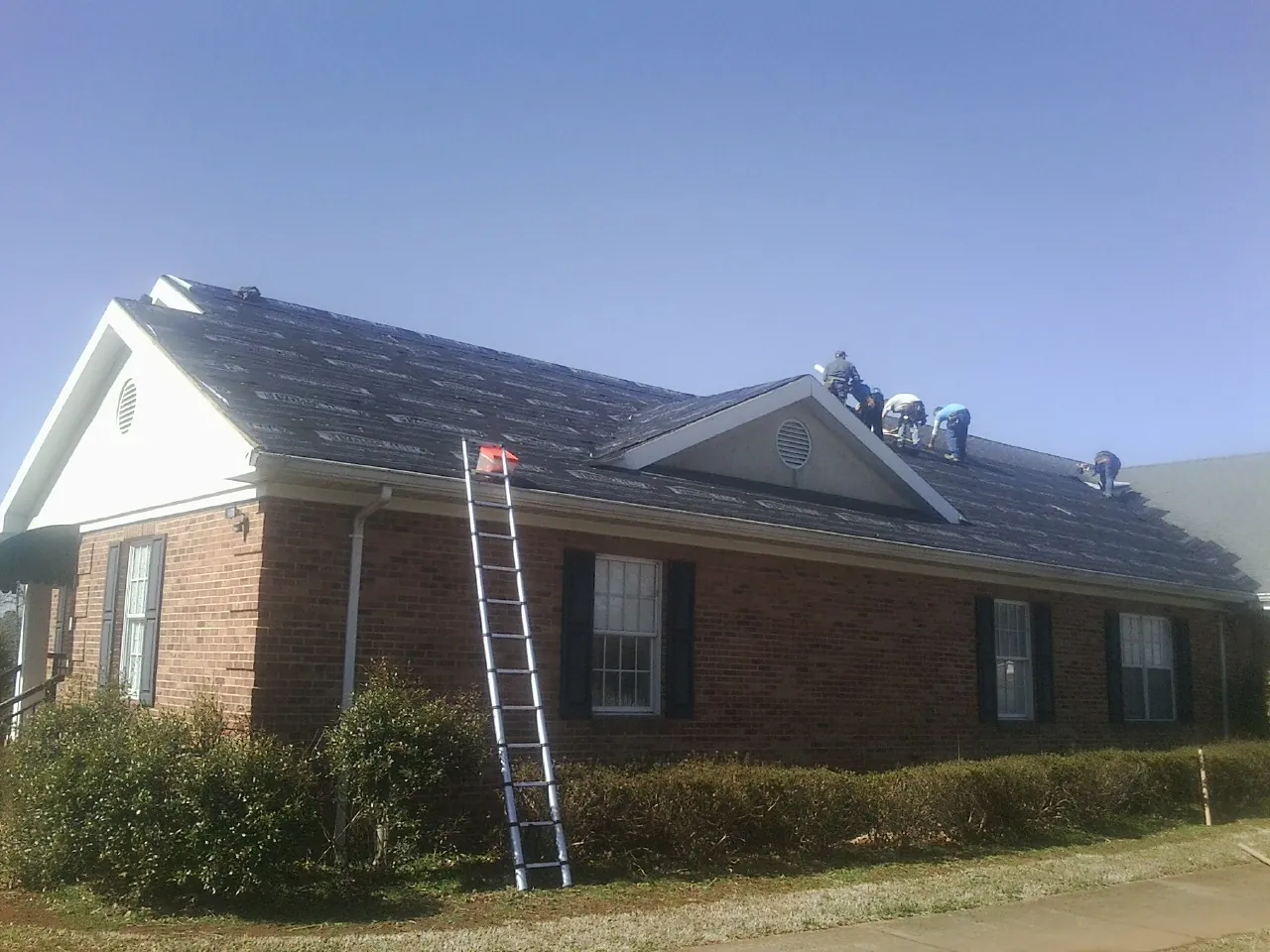 Crew tearing shingles off a brick ranch roof with a ladder set — Emergency Roof Repair work by our crew in North Berwick