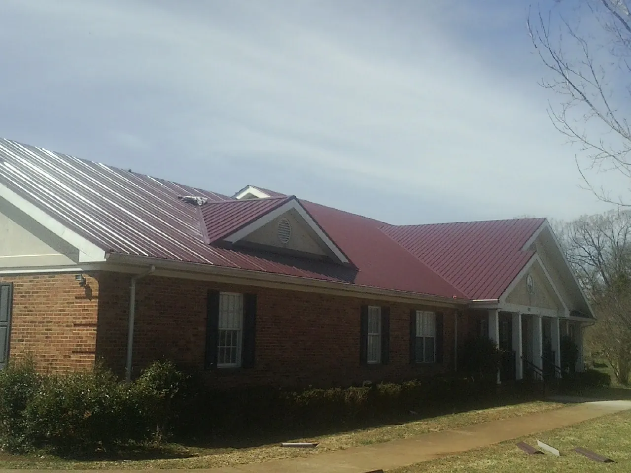 Red metal roof with gabled entries on a long brick building, from a Hail Damage Roof Repair job in North Berwick