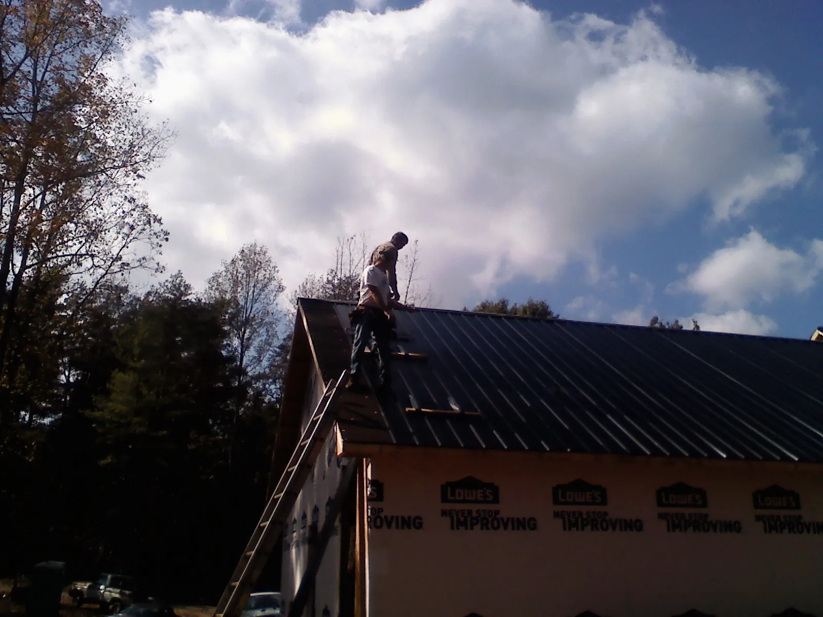 Roofer fastening dark metal panels high against a cloudy sky, from a Roof Inspection job in North Berwick